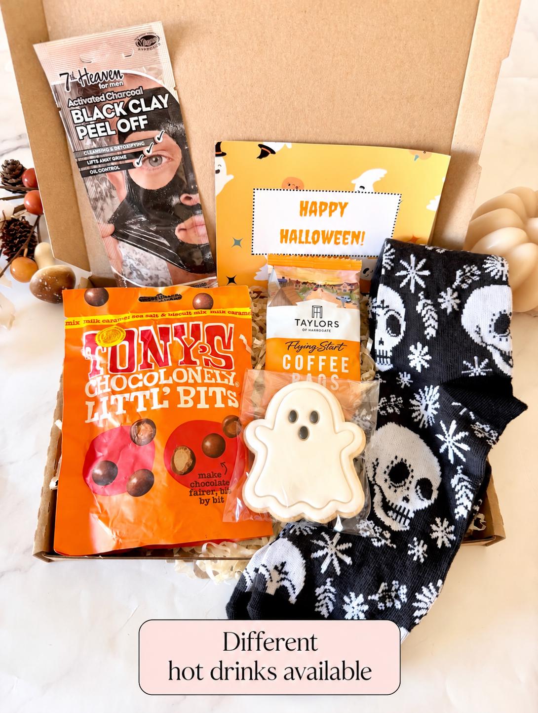 May include: A Halloween-themed gift box containing a 7th Heaven black clay peel-off mask, a bag of Tony's Chocolonely Littl' Bits, a Taylors of Harrogate coffee bag, a ghost-shaped cookie, and black socks with a white skull and snowflake pattern.